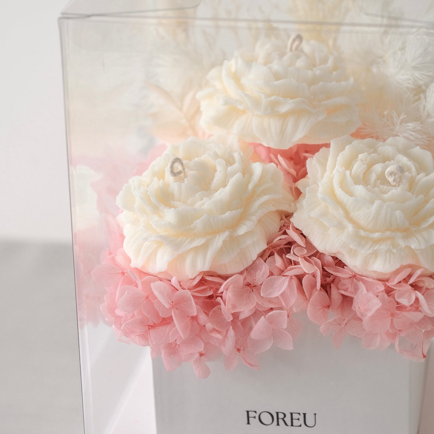 Close up image of premium flower box in the pink colourway feauturing an arrangement of preserved flowers and three scented peony shaped candles. Hydrangeas