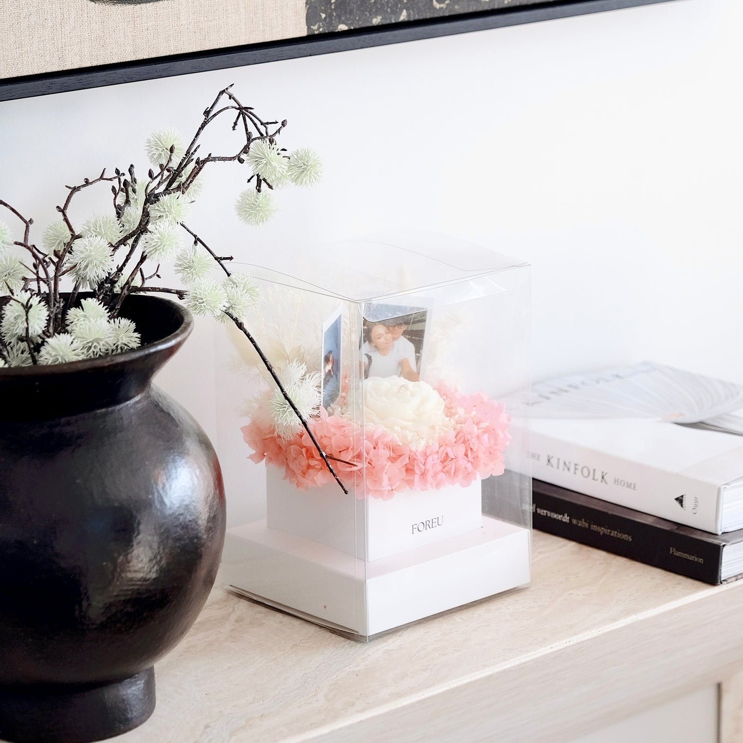 Decorative setup with a black vase, pink flowers, and books on a surface.