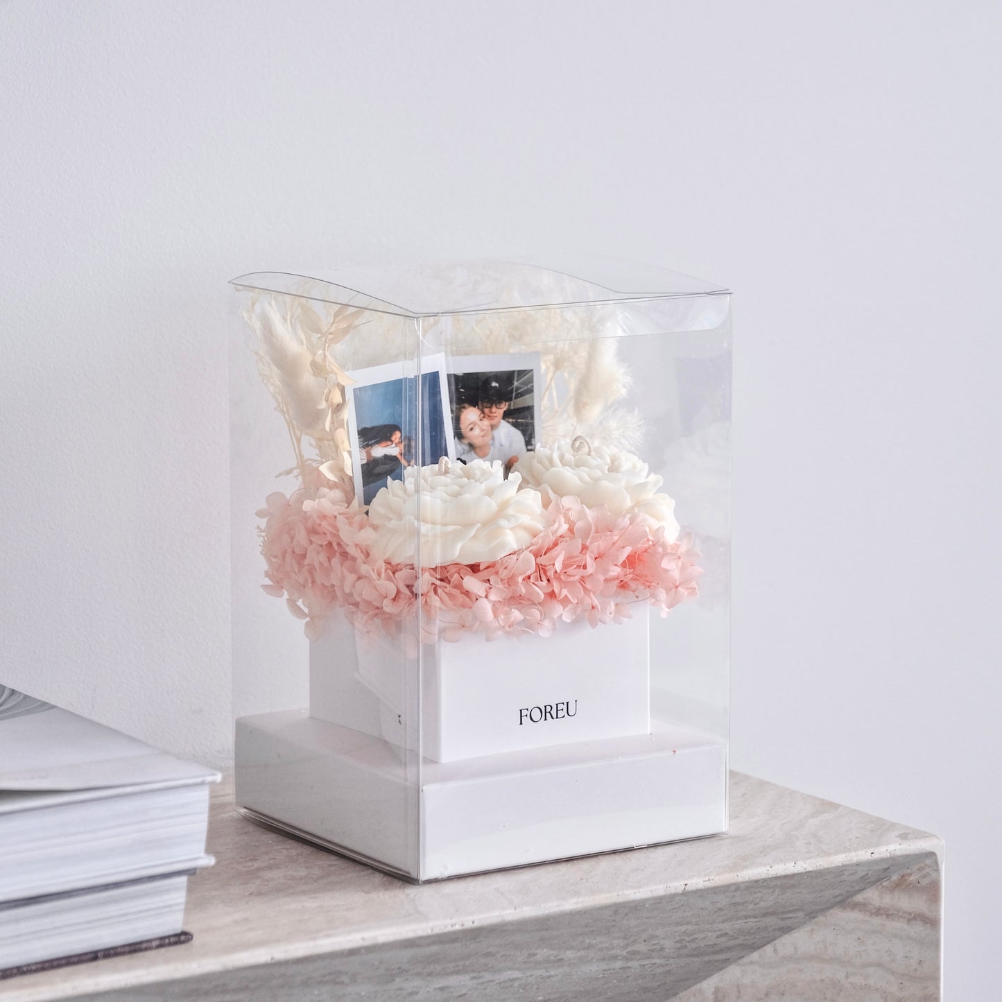 Clear box with pink and white flowers and photos on a light surface