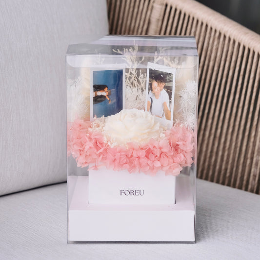 Clear decorative box with pink flowers and photos on a light background