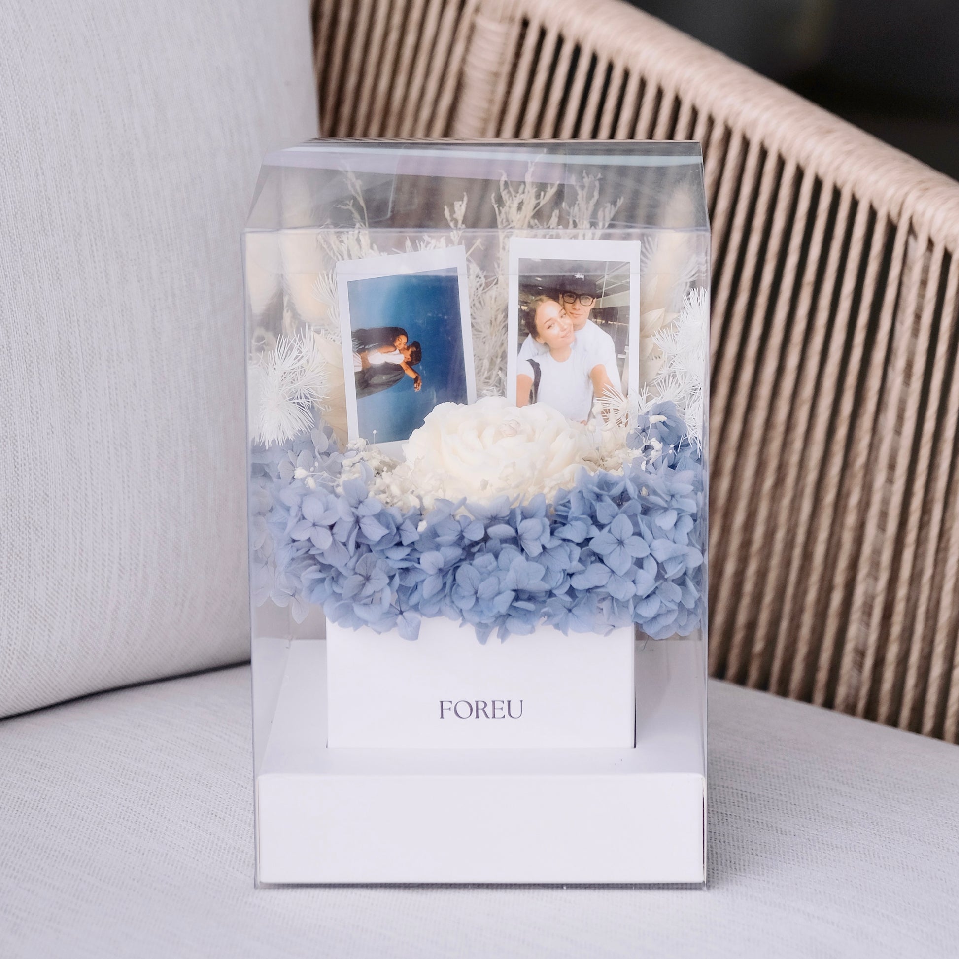 Decorative box with blue preserved flowers and custom polaroid photos on a light background
