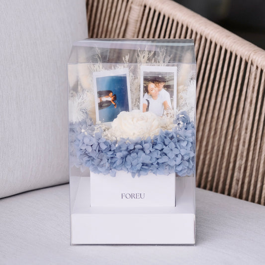 Decorative box with blue preserved flowers and custom polaroid photos on a light background