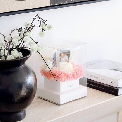 Decorative setup with a black vase, pink flowers, and books on a surface.